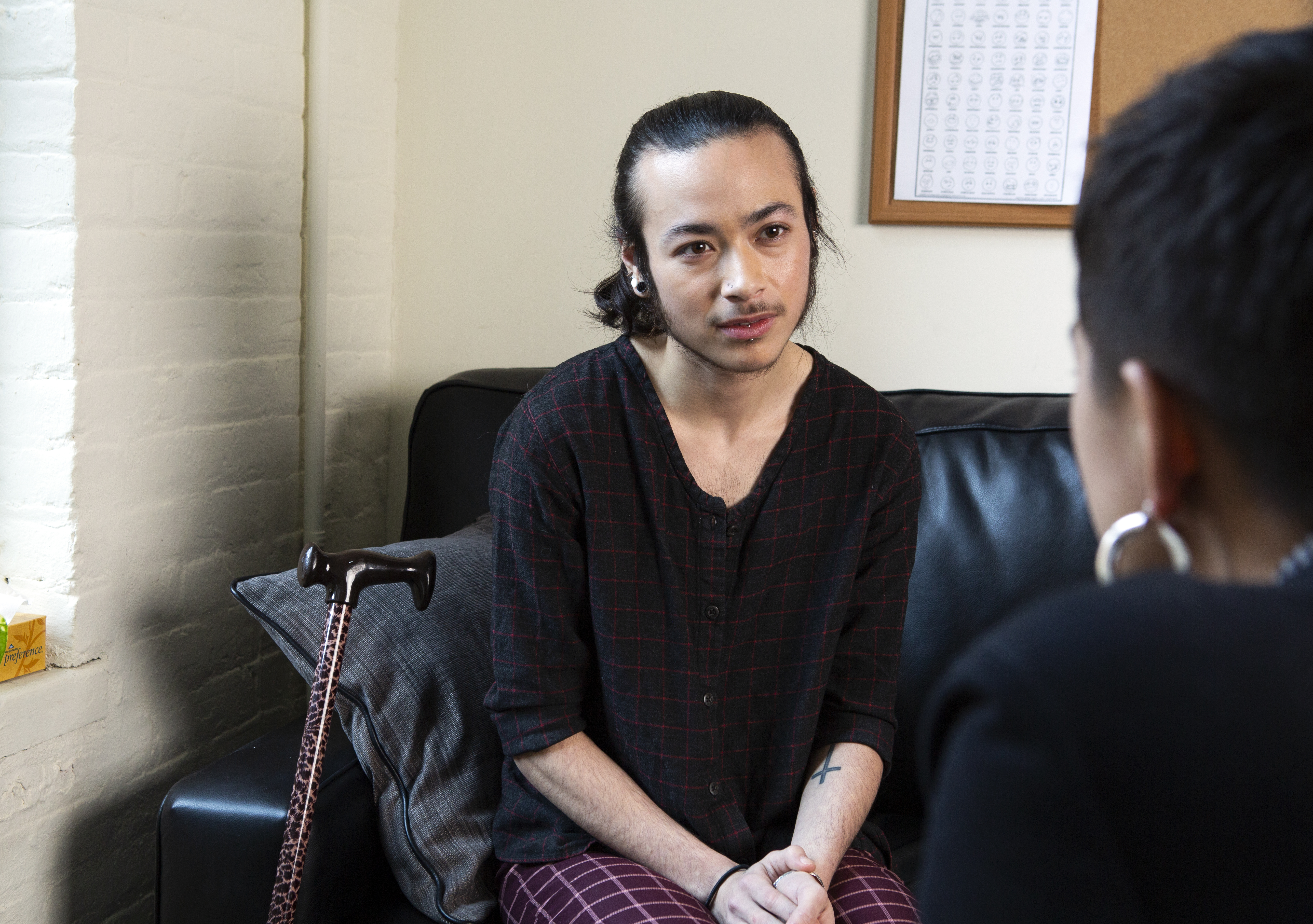 A genderqueer person sitting on a therapist's couch, listening